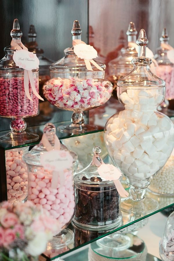 there are many different types of candy in the glass vases on the table, including pink and white lollipops