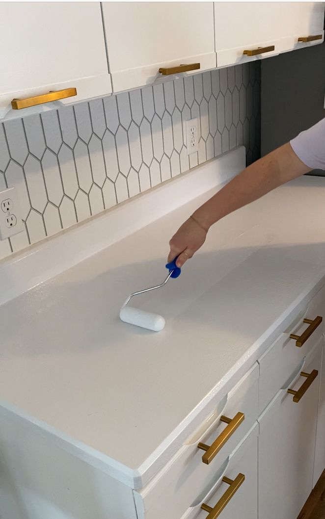 a person using a brush to clean a white counter top with gold hardware on it