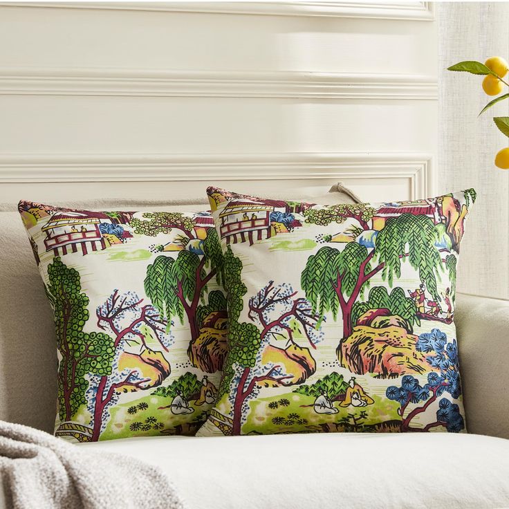 two pillows sitting on top of a white couch next to a vase with yellow flowers