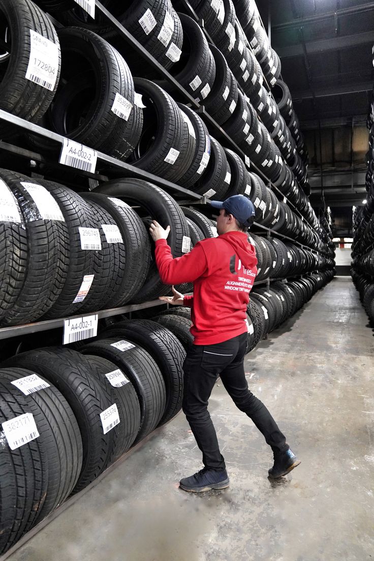 a man in a red jacket and black pants is looking at the tires on display