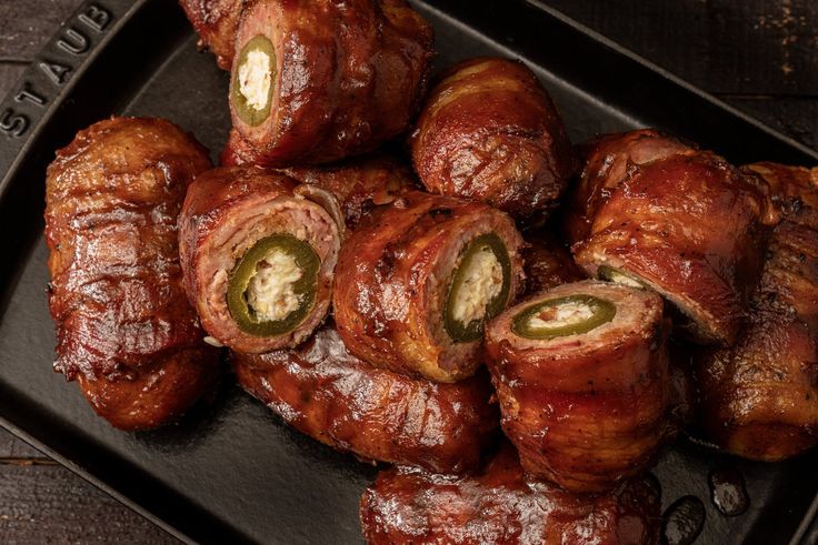 there are several sausages wrapped in bacon on a black platter with green peppers