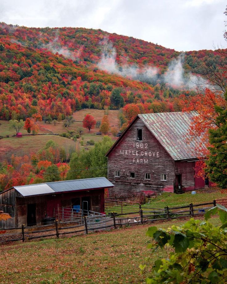 an old barn sits on the side of a hill with autumn trees in the background