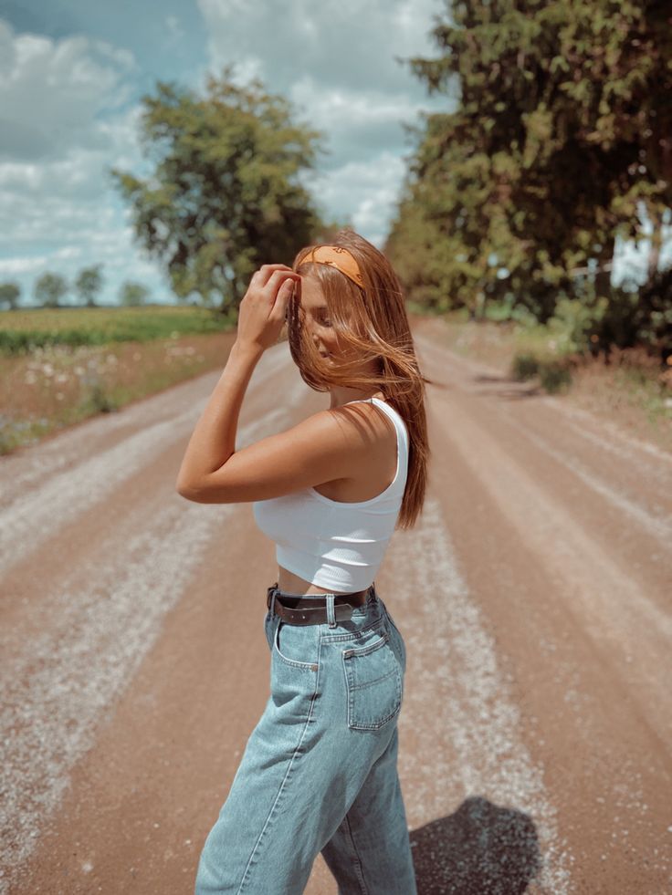 a woman standing on the side of a dirt road with her hair blowing in the wind