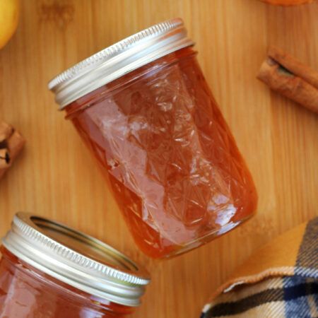 two jars filled with jam sitting on top of a wooden table next to an apple