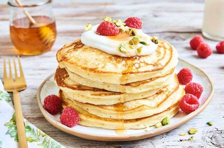 a stack of pancakes topped with whipped cream and raspberries