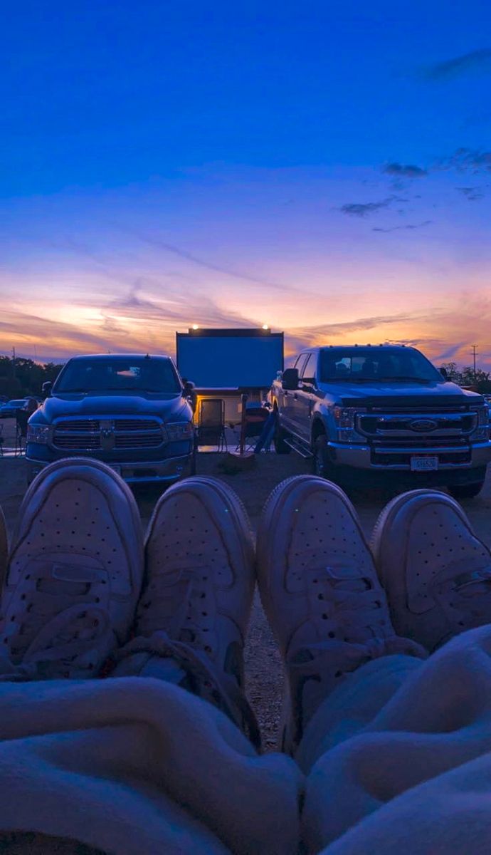 two people are sitting in front of their cars watching the movies at sunset or dawn