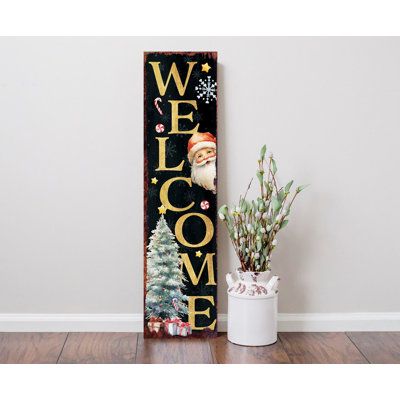 a welcome sign next to a potted plant on a wooden floor in front of a white wall