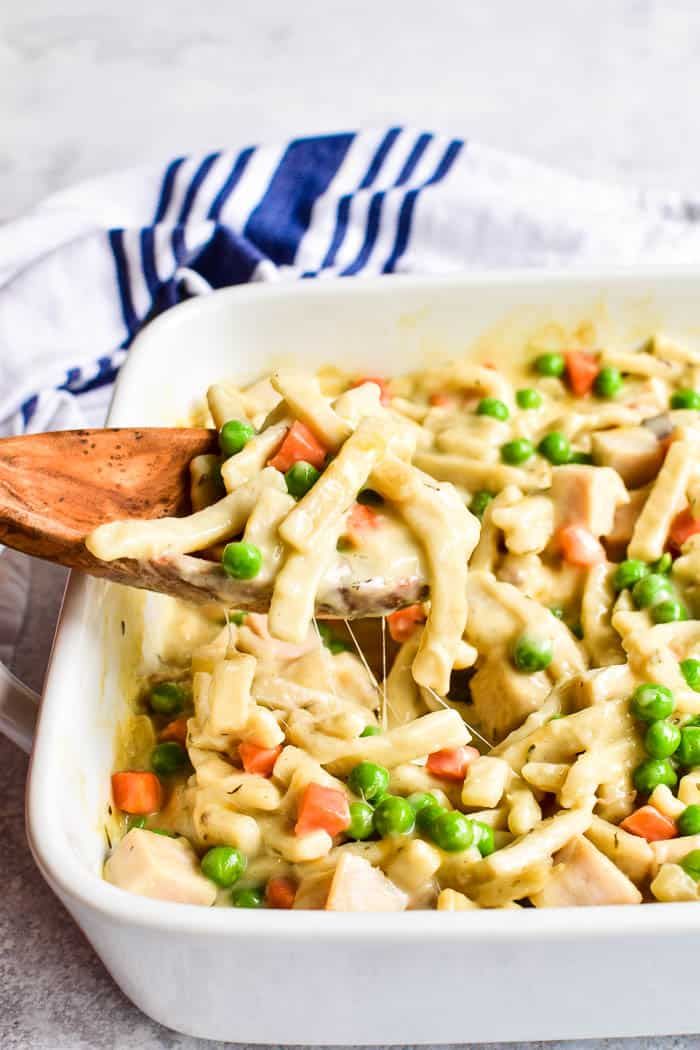 a casserole dish with peas, carrots and chicken is being stirred by a wooden spoon