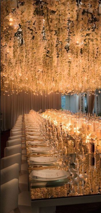 a long table with many candles and plates on it in front of a large chandelier