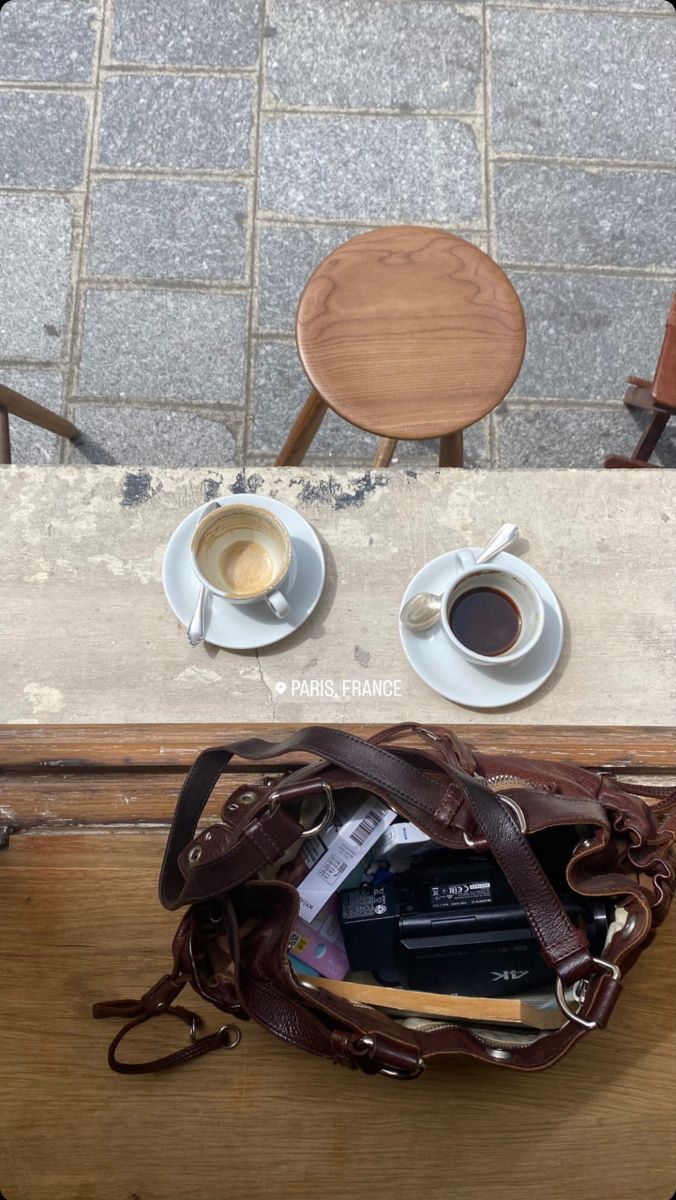 two cups of coffee sit on a table next to an open purse and a cup of espresso