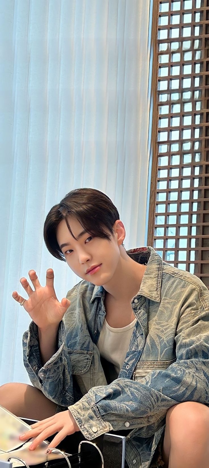 a young man sitting on top of a couch next to a window holding his hand up