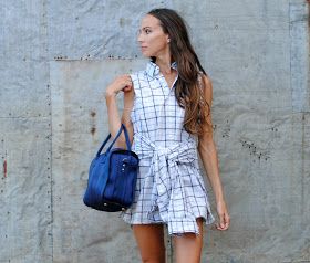 a woman is standing in front of a wall holding a blue handbag