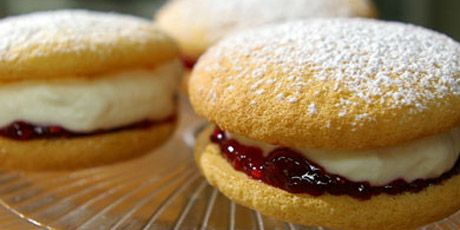 three pastries on a glass plate with powdered sugar and jelly fillings in between them