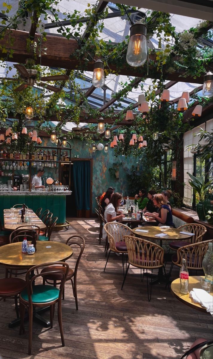 people are sitting at tables in an outdoor dining area with plants growing on the ceiling