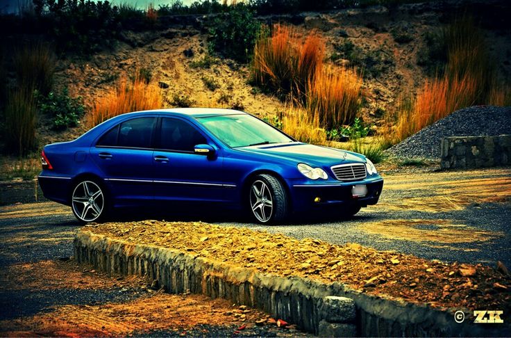 a blue car parked on the side of a road next to a hill and grass