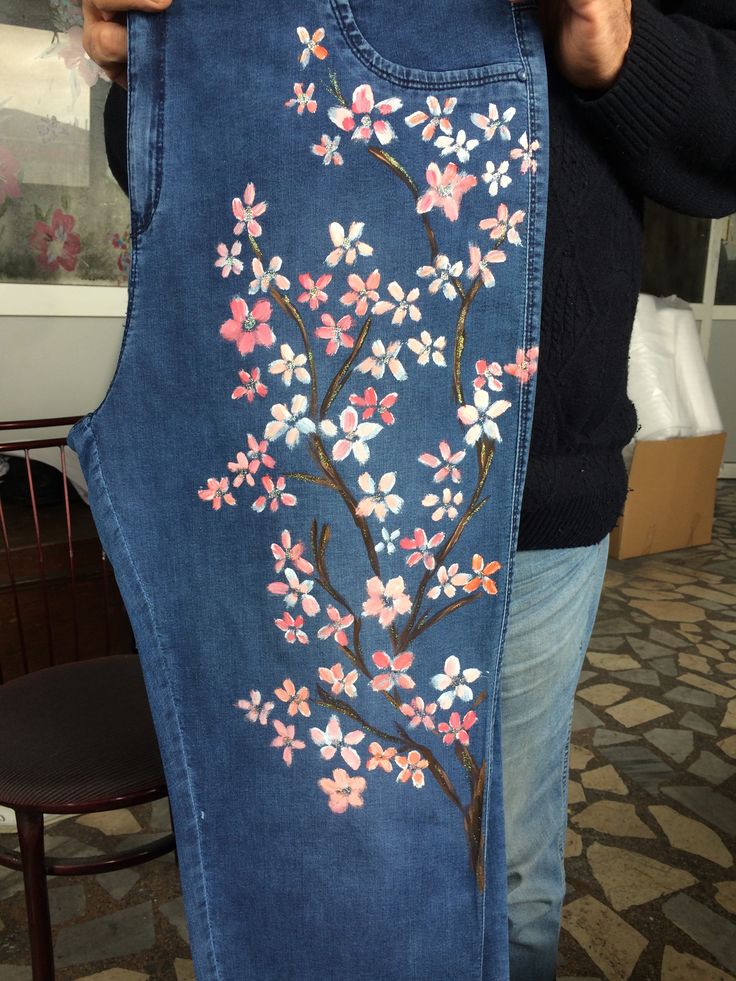 a woman holding up a piece of blue jean with pink flowers painted on the side