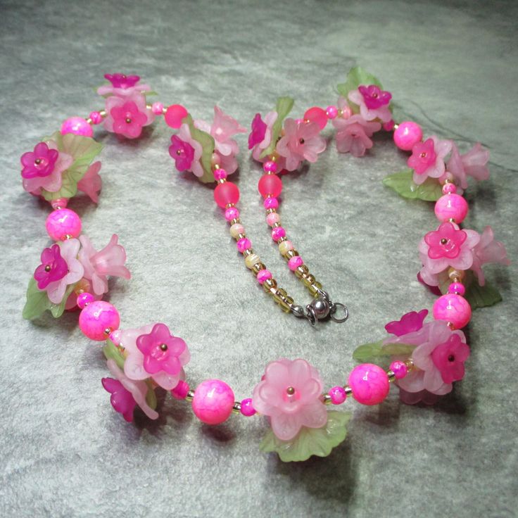 Frosted Lucite flowers in various shades of pink are layered together to make more complex flowers each with a pink seed bead at its centre and one in three with the addition of a pale green frosted Lucite leaf. Eleven triplets of these make up the front of the necklace between each triplet are two 4mm pink and yellow patterned Glass beads containing between them two 4mm pink patterned beads and a matching 10mm bead. Between the final two flowers the 10mm beads are replaced by 8mm pink frosted glass beads. At each end of the necklace are 4mm patterned Glass beads alternatively pink and pink/yellow, all these flowers and beads are separated by silver lined pale gold Glass seed beads. All the metal work is Stainless Steel including the magnetic clasp and the earwires on the free matching ear Beaded Flower Necklace For Spring, Summer Pink Flower Beaded Necklaces, Pink Flower Necklace For Summer Gift, Summer Pink Flower Necklace As A Gift, Adjustable Pink Flower-shaped Necklace, Pink Adjustable Flower Shaped Necklace, Pink Beaded Flower-shaped Jewelry, Pink Petal-shaped Jewelry For Spring, Summer Pink Jewelry With 3d Flowers