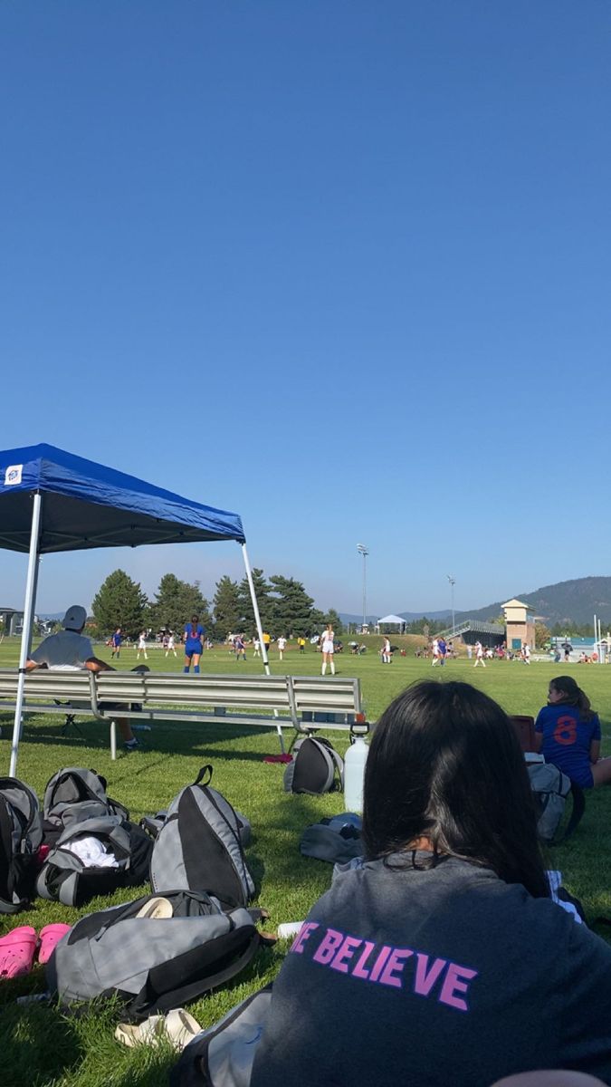 people are sitting on the grass under a blue tent