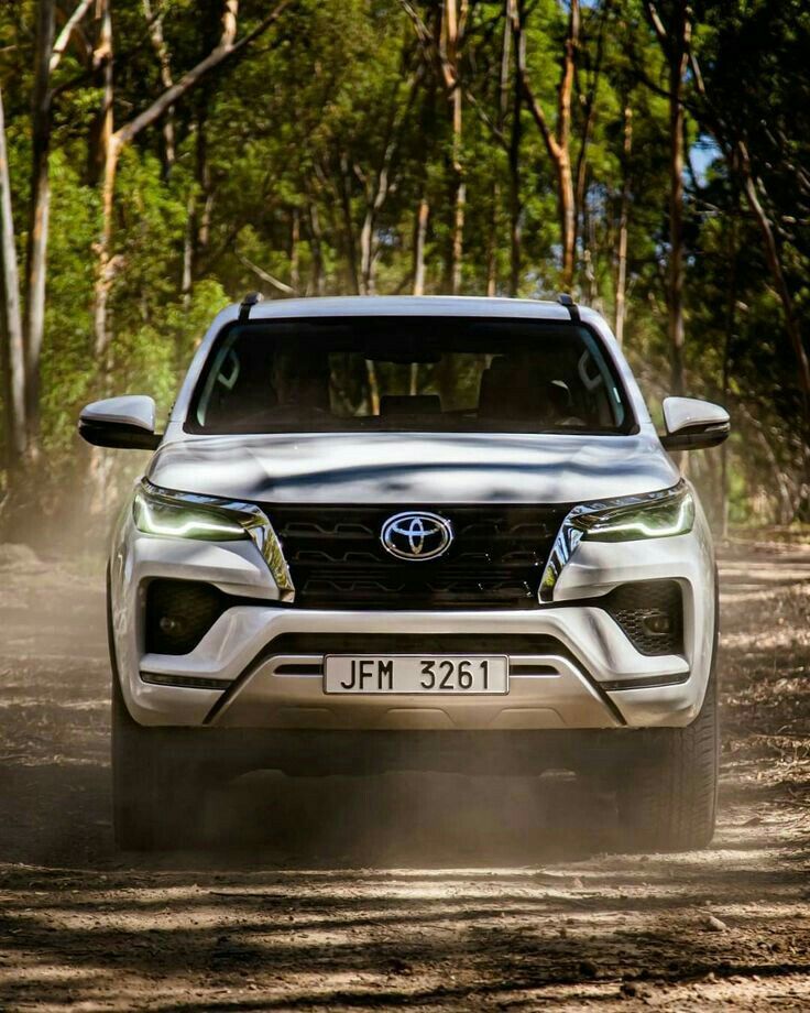 the front end of a silver toyota pickup truck driving down a dirt road with trees in the background