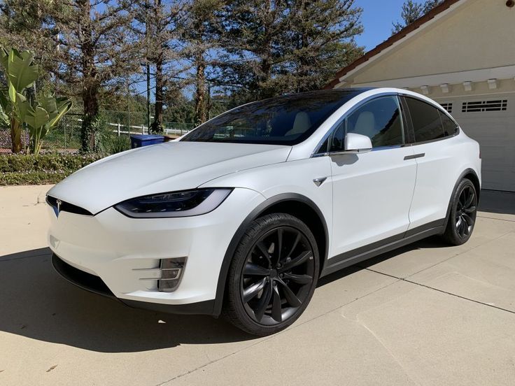 a white tesla model x parked in front of a house with black wheels and rims