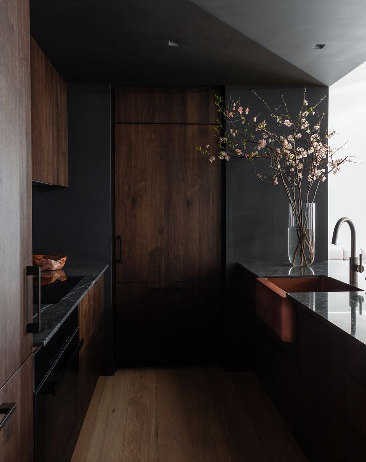 a kitchen with dark wood cabinets and black counter tops is pictured in this image, there are flowers in a vase on the counter