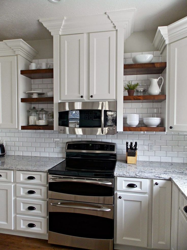 a kitchen with white cabinets and stainless steel stove top oven in the center, surrounded by open shelving