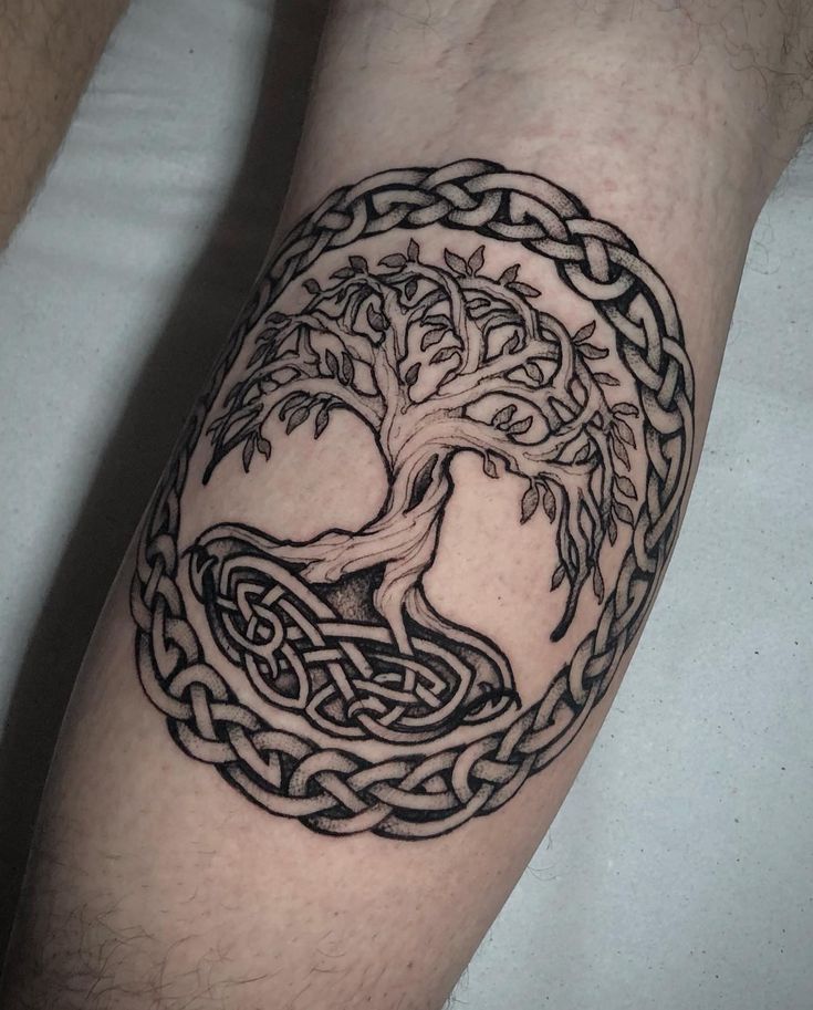 a man's arm with a tree and celtic knot tattoo on the side of his leg