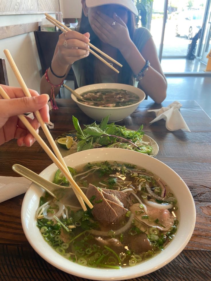 two women eating soup with chopsticks at a table