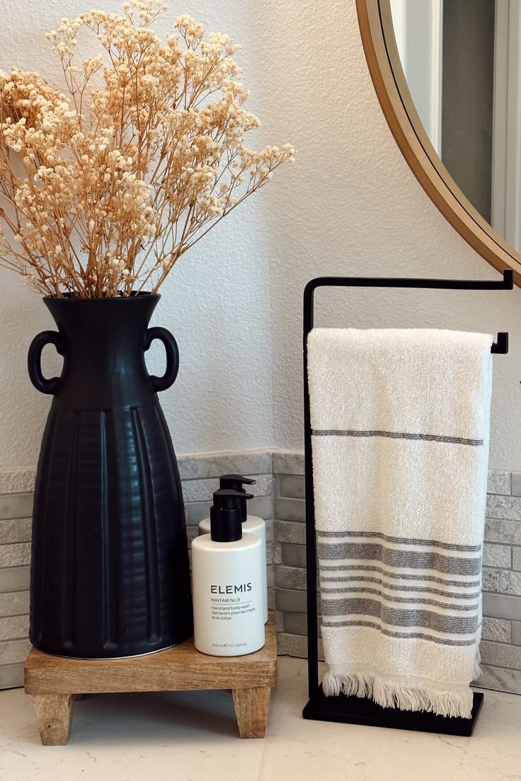 a black vase sitting on top of a counter next to a white towel and bottle