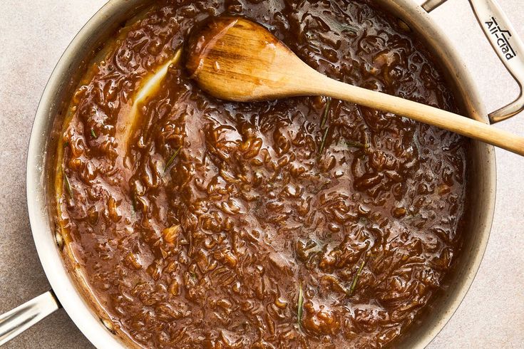 a wooden spoon in a pot filled with food and sauce on a table next to utensils