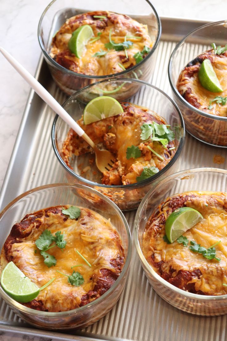 four glass bowls filled with food on top of a metal serving tray next to lime wedges