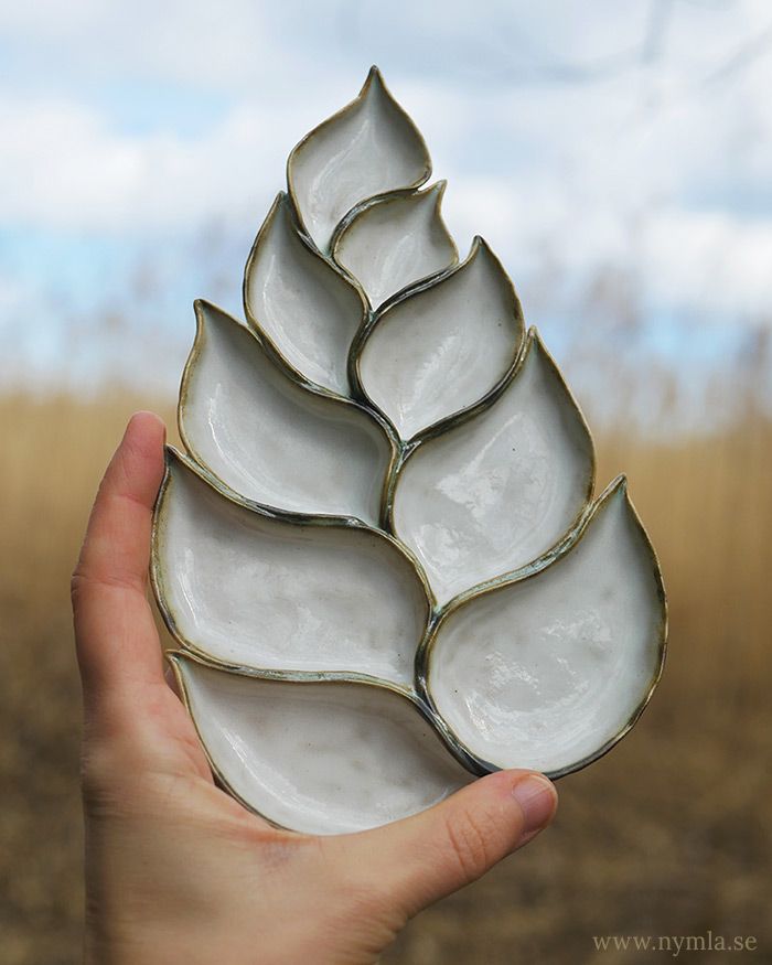 a hand holding a white and gold decorative object in the middle of a grassy field