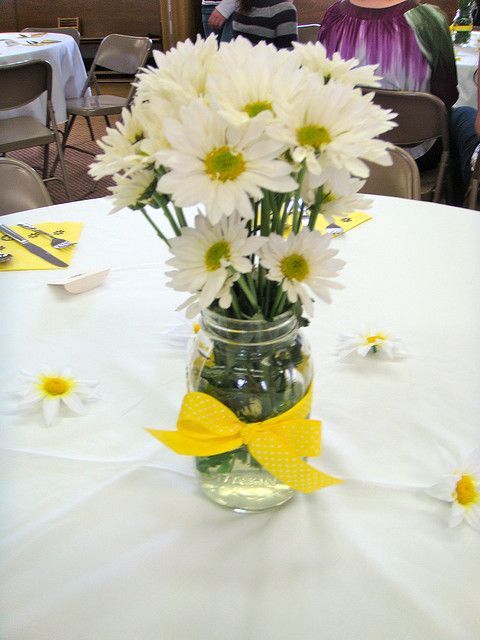 a vase filled with white and yellow flowers on top of a table next to people