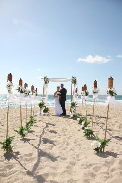 a newly married couple standing under an arch on the beach