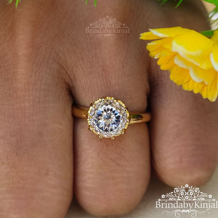 a woman's hand with a ring on it and yellow flowers in the background