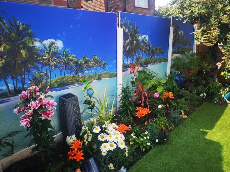 there are many flowers and plants in the garden by the wall that is decorated with palm trees