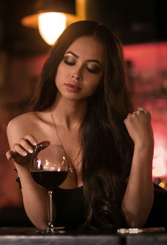 a woman sitting at a table with a glass of wine in front of her face