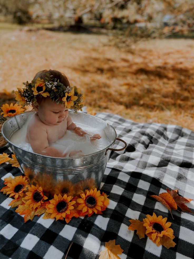 a baby is taking a bath in a bucket with sunflowers on the table