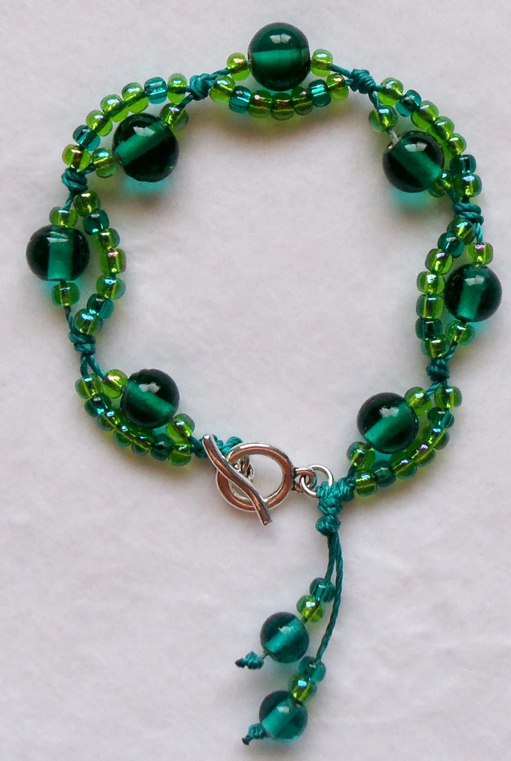 a green beaded bracelet with silver clasp and beads on it's end, sitting on a white surface