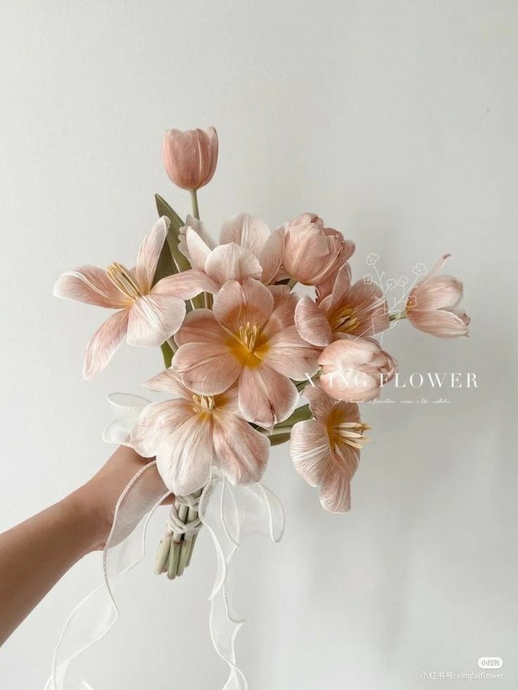 a bouquet of pink flowers being held by a person's hand against a white wall