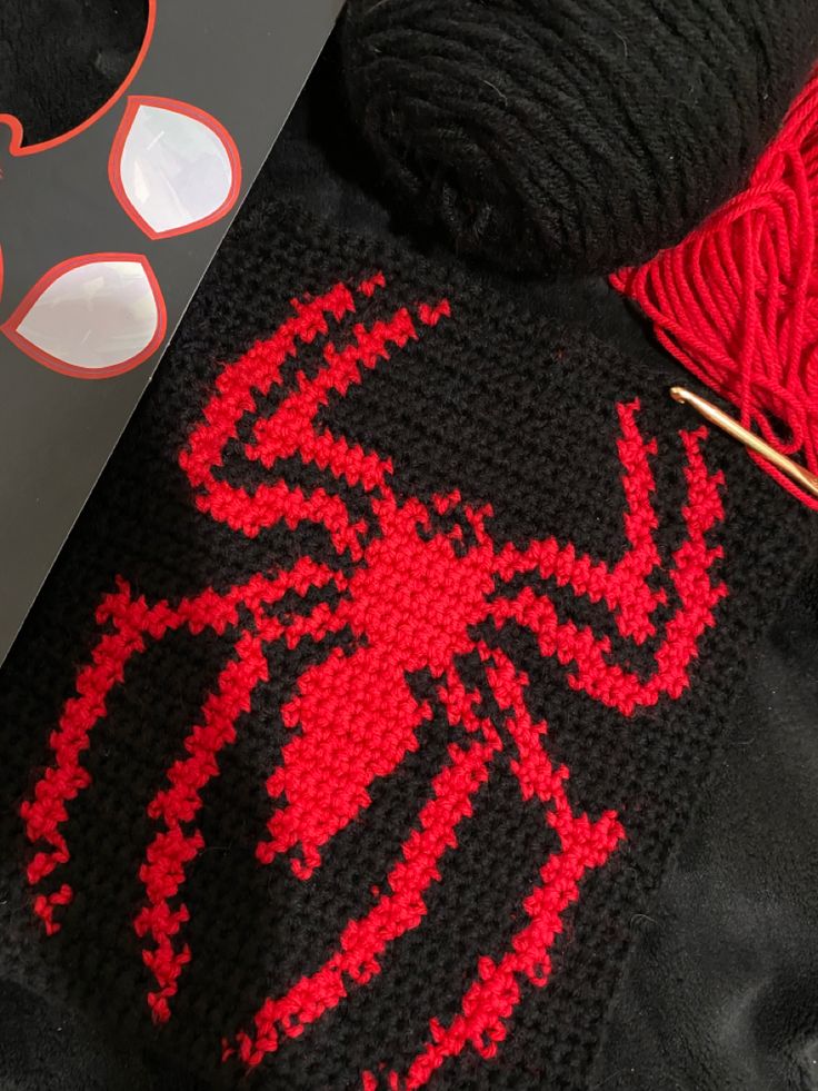 a red spiderman crocheted sweater next to yarn and knitting needles