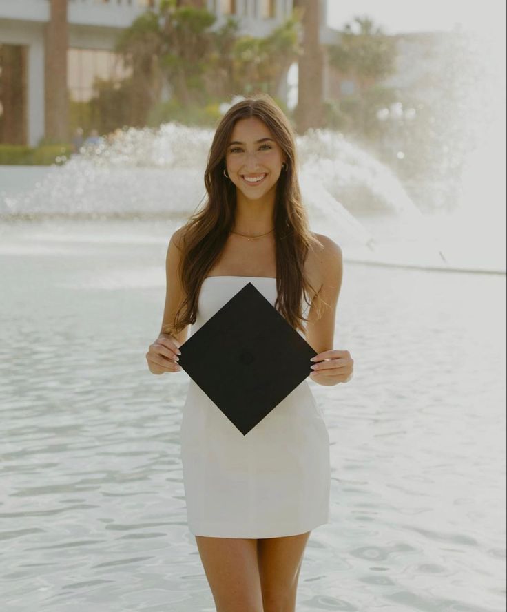 a beautiful young woman standing in front of a fountain holding a black and white square