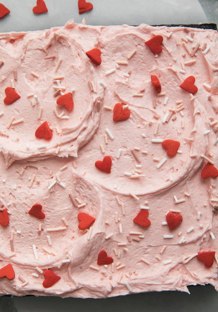 a cake with pink frosting and red hearts on it's icing sheet