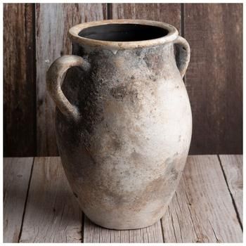 an old stone vase sitting on top of a wooden table next to a wall with wood planks