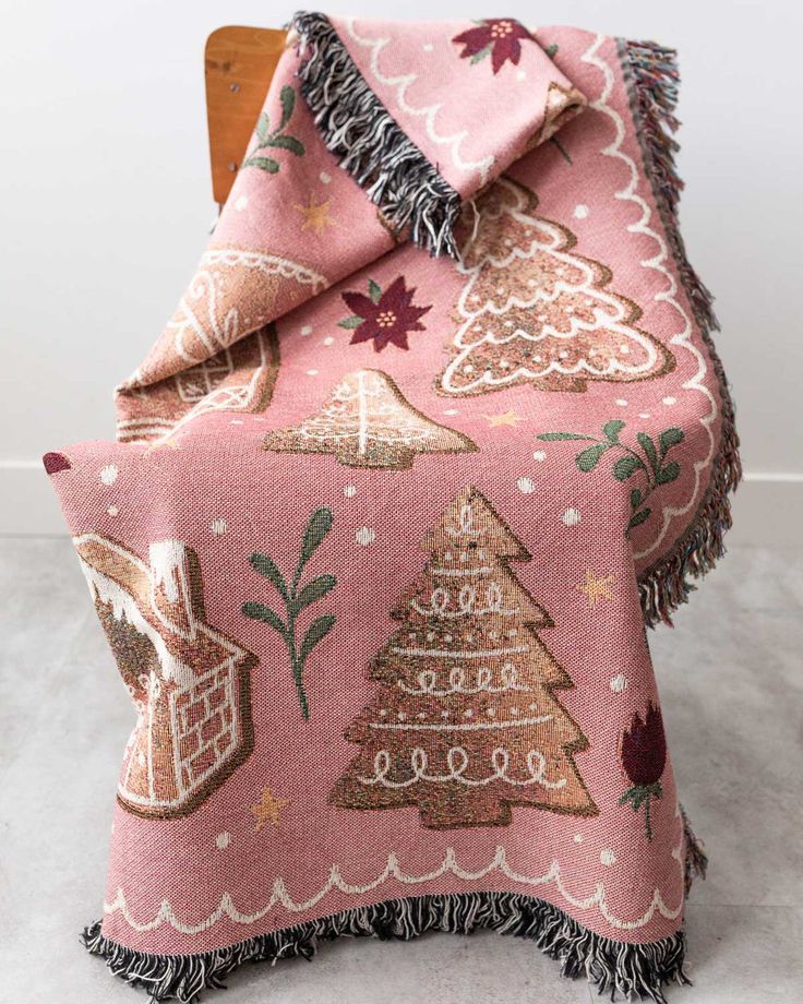 a pink blanket with christmas trees on it and fringes around the edges, sitting on top of a wooden chair