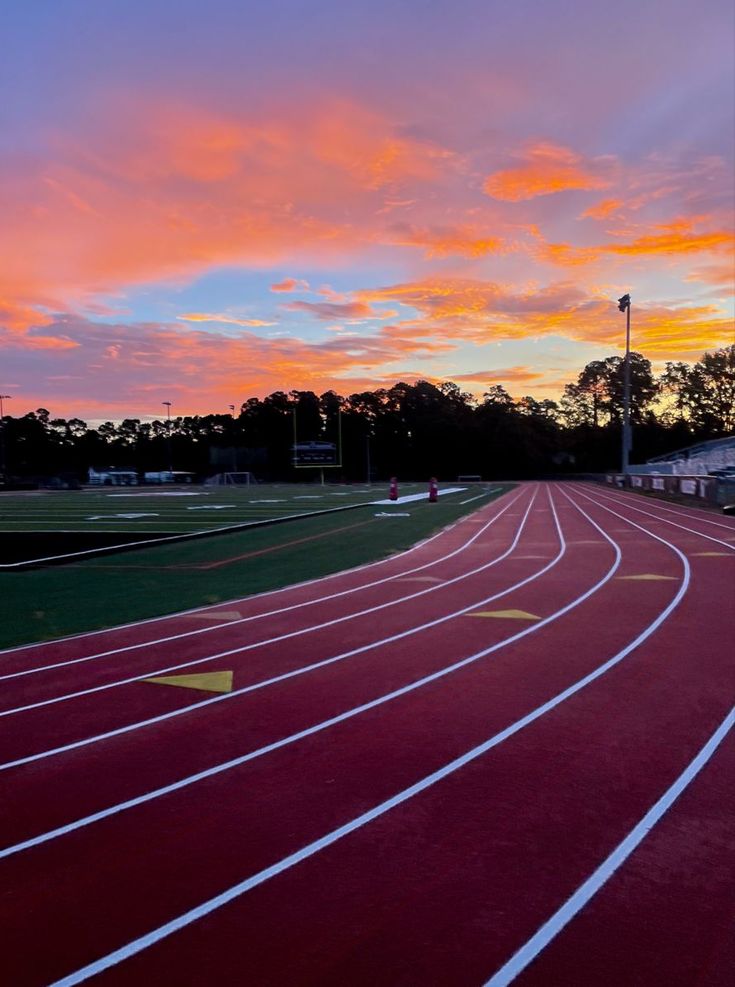 the sun is setting over a running track with red and white lines on it,