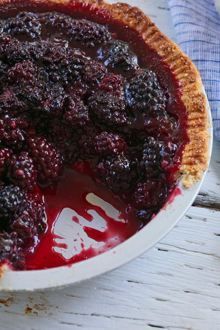 a pie with blueberries in it sitting on a white plate next to a napkin