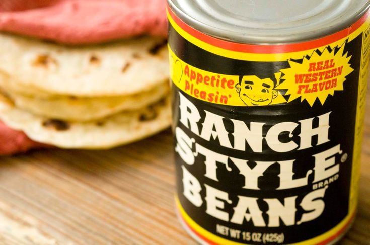 a can of ranch style beans sitting on top of a wooden table next to some pita bread