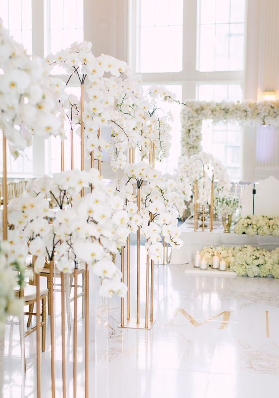 a room filled with lots of white flowers and gold vases next to each other