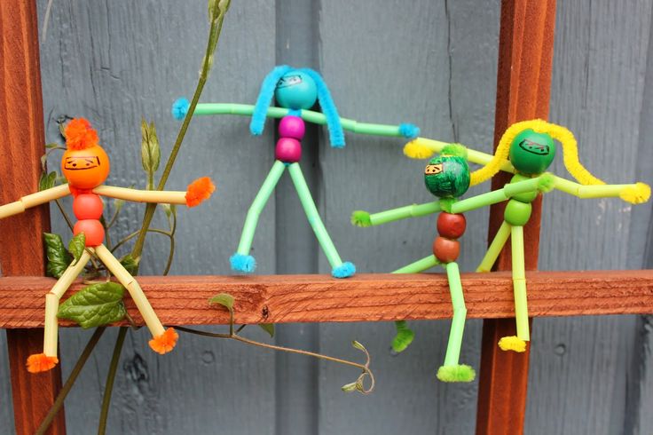 three plastic dolls are hanging on a wooden fence with flowers in the foreground and one is holding a plant